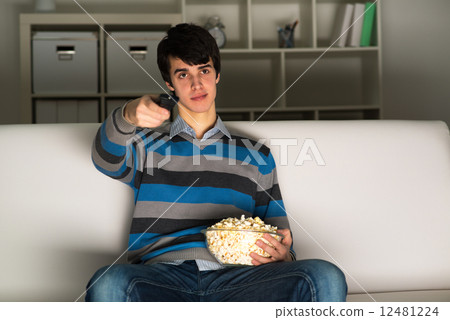young man watching television with popcorn 12481224