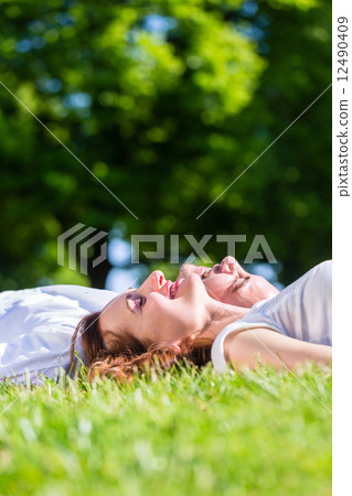 Friends laying side by side on park lawn enjoying sun 12490409