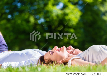 Friends laying side by side on park lawn enjoying sun Friends laying side by side on park lawn enjoying sun 12490410