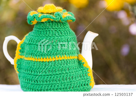 Knitted doily on the teapot on a natural background. 12503137