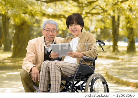 Senior couple walking by wheelchair in autumn park 12508560