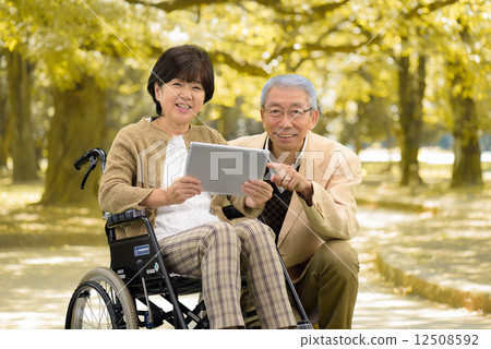 Senior couple walking by wheelchair in autumn park Senior couple walking by wheelchair in autumn park 12508592