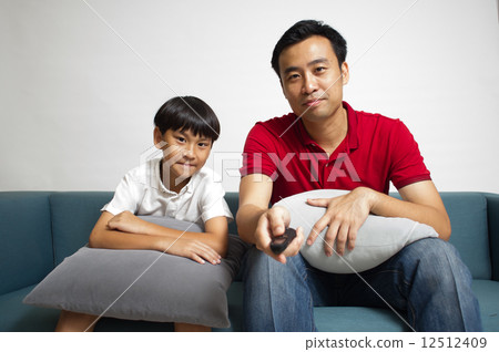 Asian father and son watching television drama together in the living room 12512409