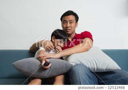 An Asian father and son got scare and  embraced together watching TV horror show in the living room 12512466