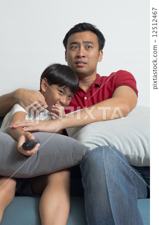 An Asian father and son got scare and  embraced together watching TV horror show in the living room 12512467