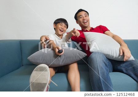 An Asian father and son having a good laugh watching TV comedy program in the living room An Asian father and son having a good laugh watching TV comedy program in the living room 12512468