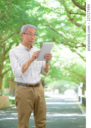 Senior men taking a walk on a fresh green ginkgo tree row while looking at the tablet Senior men taking a walk on a fresh green ginkgo tree row while looking at the tablet 12517484