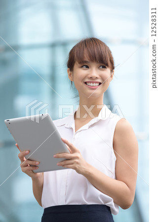 Young successful Chinese business woman using mobile device tablet iPad in front of office building 12528311
