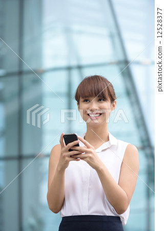 Young successful Chinese business woman using smart phone in front of glass office building Young successful Chinese business woman using smart phone in front of glass office building 12528377