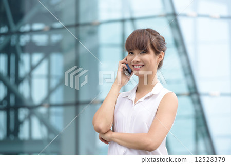 Young successful Chinese business woman making voice call in front of glass office building 12528379