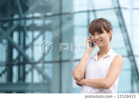 Young successful Chinese business woman making voice call in front of glass office building Young successful Chinese business woman making voice call in front of glass office building 12528413