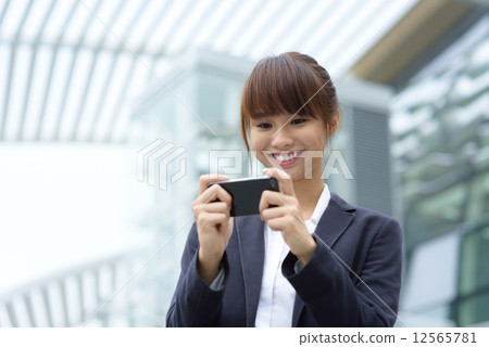 One young Chinese office lady using smart phone in front of office building One young Chinese office lady using smart phone in front of office building 12565781