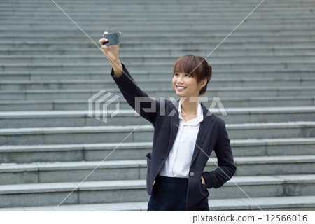 One young chinese office lady taking selfies with her smart phone in front of steps 12566016