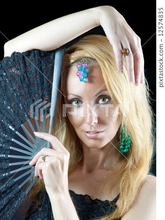 The beautiful young woman with long  blonde hair and  fan and jewellry on  dark background 12574835