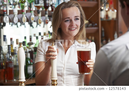 Female Bartender Serving Drink To Male Customer 12578143