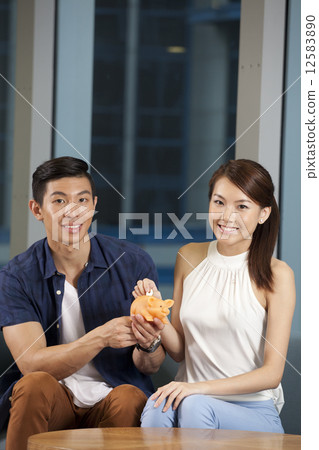 Asian couple on sofa with piggy bank 12583890