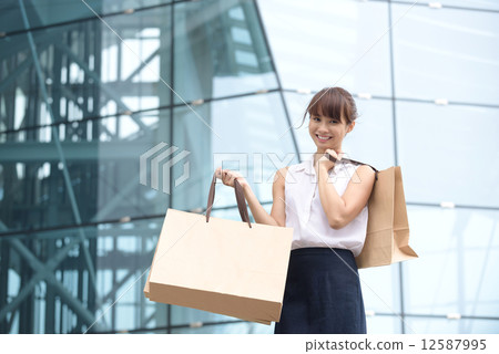 One young chinese shopaholic with her shopping buys in front of glass building mall 12587995