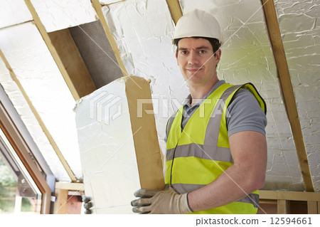 Builder Fitting Insulation Boards Into Roof Of New House 12594661
