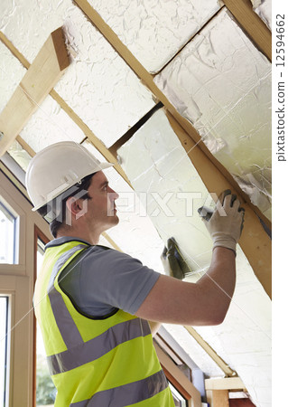 Builder Fitting Insulation Boards Into Roof Of New Home 12594662