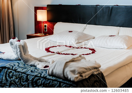 Honeymoon bed decorated with red rose petals and towels 12603485