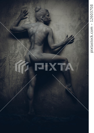 Naked sportive woman painted in grey color posing over grey wall 12603708