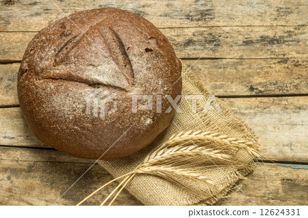 Loaf of bread with wheat grains on wooden background 12624331