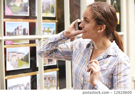 Happy Young Woman On Phone Outside Estate Agents 12628600