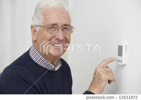 Smiling Senior Man Adjusting Central Heating Thermostat Smiling Senior Man Adjusting Central Heating Thermostat 12631872