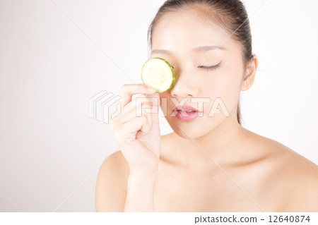 Asian young beautiful woman with flawless complexion holding cucumber slice over eye Asian young beautiful woman with flawless complexion holding cucumber slice over eye 12640874