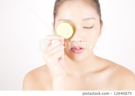 Asian young beautiful woman with flawless complexion holding cucumber slice over eye Asian young beautiful woman with flawless complexion holding cucumber slice over eye 12640875