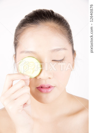 Asian young beautiful woman with flawless complexion holding cucumber slice over eye close up 12640876