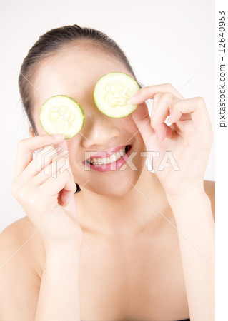 Asian young beautiful smiling woman with flawless complexion holding cucumber slices over eye 12640953
