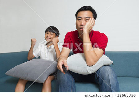 Asian Father and son watching sport supporting different team in the living room 12669336