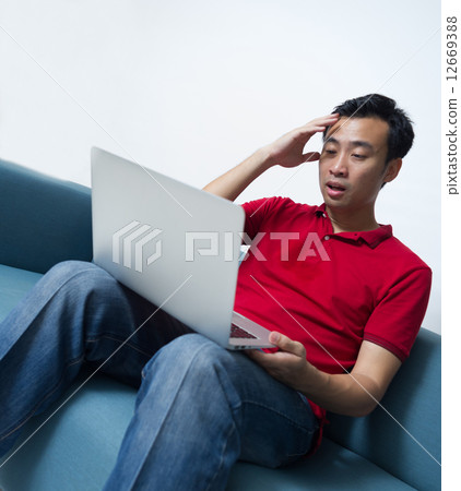 Asian male feeling troubled after receiving bad news from his latop 12669388
