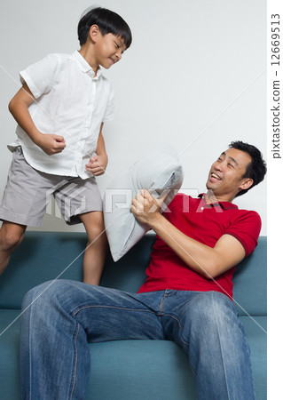 Asian boy is playing - pillow fight - with his dad / father on the sofa in the living room Asian boy is playing - pillow fight - with his dad / father on the sofa in the living room 12669513