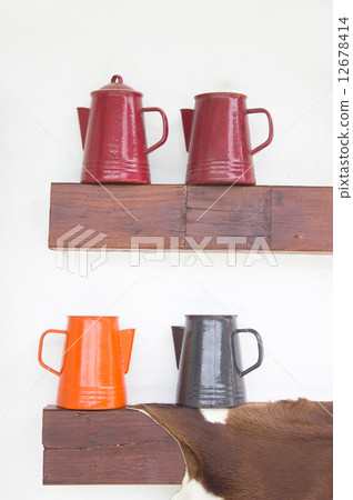 Colorful metal jugs on wooden shelf. 12678414