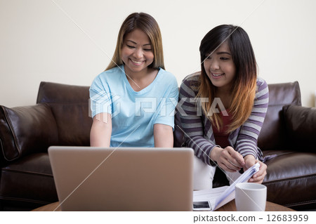 Two Asian female friends sitting at home, using a laptop pc. 12683959