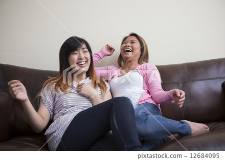Two Asian female friends at home laughing. Two Asian female friends at home laughing. 12684095