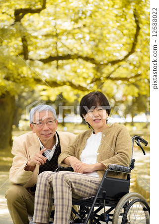 A couple who talks with each other in a wheelchair at a park of autumnal leaves A couple who talks with each other in a wheelchair at a park of autumnal leaves 12688022
