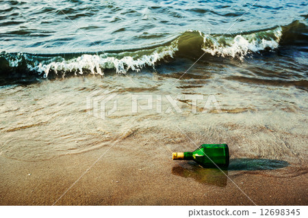 Message bottle on beach in waves 12698345