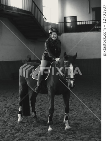 Monochrome  photo of beautiful woman riding horse in manege 12701937
