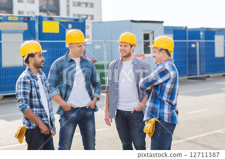 group of smiling builders in hardhats outdoors group of smiling builders in hardhats outdoors 12711387