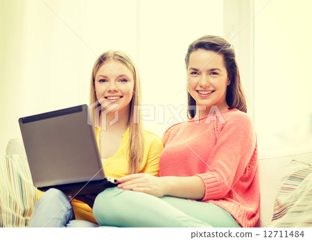 two smiling teenage girls with laptop at home 12711484