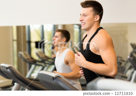 smiling men exercising on treadmill in gym 12711810