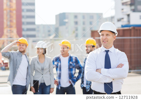 group of smiling builders in hardhats outdoors group of smiling builders in hardhats outdoors 12711928
