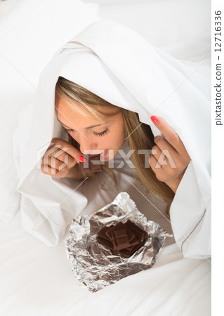 Woman eating chocolate in bed Woman eating chocolate in bed 12716336