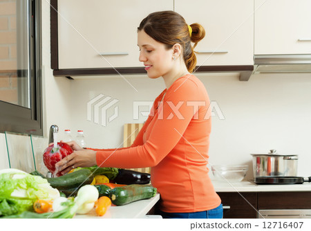 young woman washing vegetables in sink 12716407
