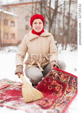 Stock Photo: woman in cap cleans carpet with snow