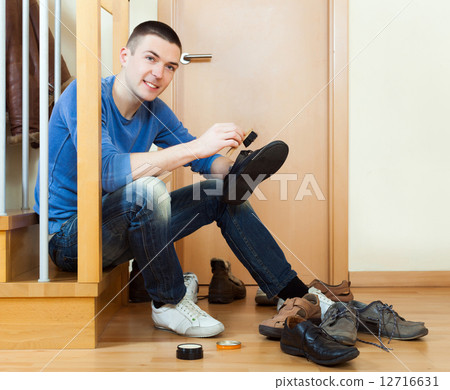 Happy man sitting on stairs and cleaning footwear 12716631