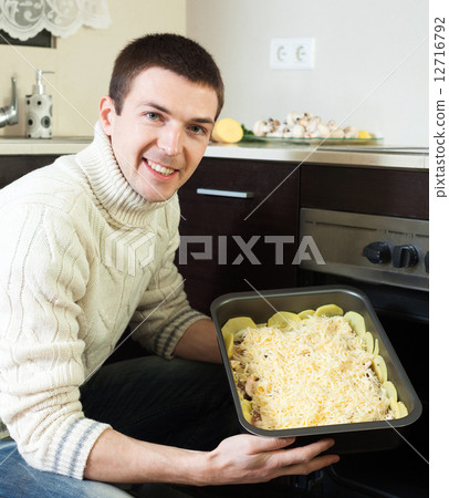 handsome man cooking french-style meat. Adding grating cheese handsome man cooking french-style meat. Adding grating cheese 12716792